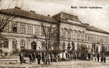 Szkoła lata 30. | Szkoła podstawowa (wtedy &bdquo;powszechna&rdquo;) w Kętach. Zdjęcie pochodzi albo z końca lat 20. XX wieku albo początku lat 30. Świadczy o tym pomnik grunwaldzki z 1910 r., parkan i dość już wyrośnięte drzewa. Na pierwszych fotografiach nie było i