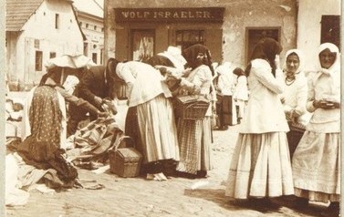 Handlujące w Rynku kobiety stoją przed żydowskim sklepem Wolfa Israelera, kt&oacute;ry handlował obuwiem. Dziś w tym miejscu jest &bdquo;Rycerska&rdquo;.