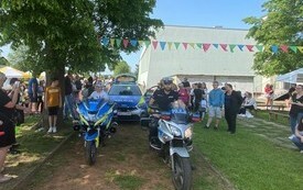 KP Kęty. Piknik przy SP nr 2 w Kętach dziecko i policjant siedzą na motocyklach w tle radiow&oacute;z i budynek