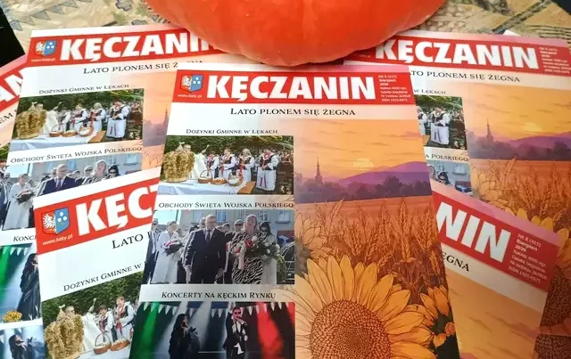 Kilka gazet "Kęczanin" rozsypanych na stole, powyżej dynia