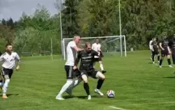 Piłkarze w trakcie gry na stadionie: Jeden próbuje odebrać piłkę drugiemu, w tle i obok pozostali gracze