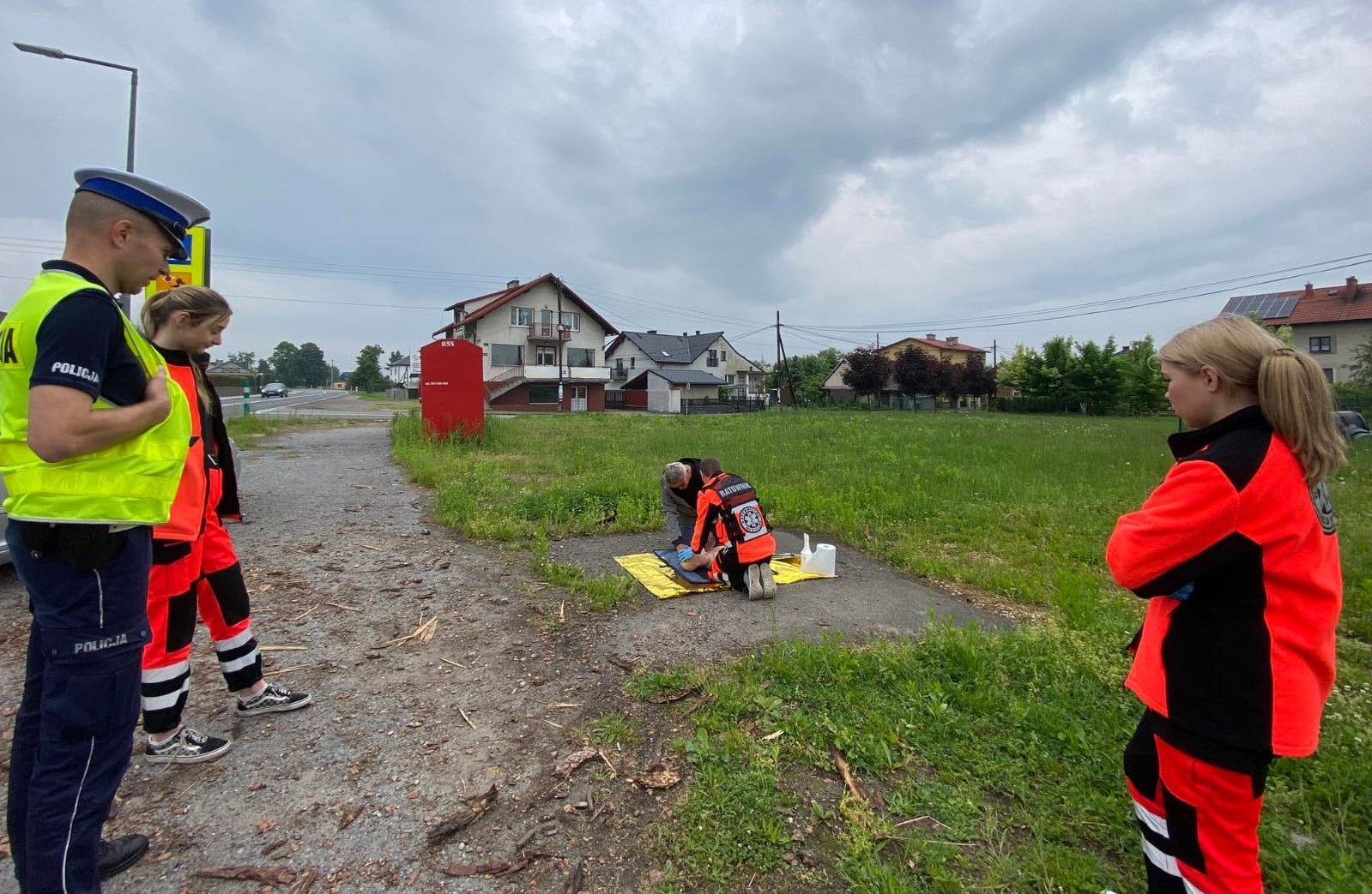 KPP_Oświęcim-_Akcja_na_rzecz_bezpieczeństwa_w_ruchu_drogowym_Dzień_Matki_nauczycielratownictwa_pokazuje_kierowcy_w_jaki_sposób_prowdzić_resuscytację_obok_stoją_uczennice_i_policjant