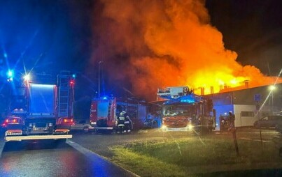 Na zdjęciu widoczny jest pożar hali w Malcu - na pierwszym planie widoczne są pojazdy Straży Pożarnej, w tle płonące budynki