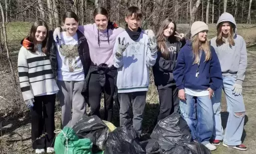 Siedmioro uczniów w rękawicach roboczych prezentujących kilka pełnych worków na śmieci