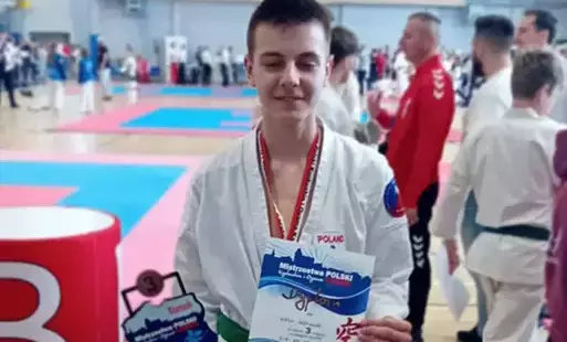 Chłopiec w kimono pozujący do zdjęcia ze statuetką i dyplomem 