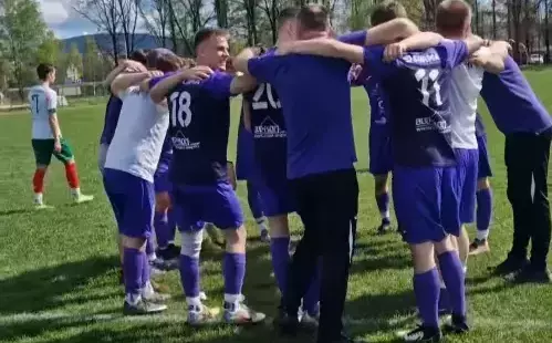 Piłkarze na murawie, stoją w kręgu, obejmując się ramionami