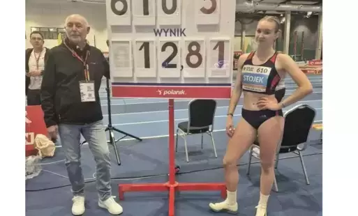 Mężczyzna i dziewczyna, ona w stroju sportowym, pozują do wspólnego zdjęcia na tle tablicy z wynikiem