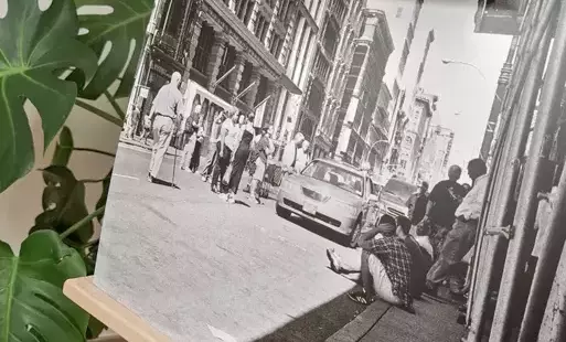 czarno-białe zdjęcie prezentujące fotografię z wystawy: nowojorczycy siedzą na ulicy, spanikowani i niepewni co się dzieje, w tle kłęby dymu ze zniszczonych wież WTC, uszkodzonych w ataku 11 września 2001 roku w Nowym Jorku