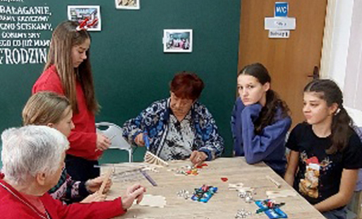 uczniowie i seniorzy z domu senior wigor w kętach siedzą przy stole i pracują nad projektami przy warsztatach