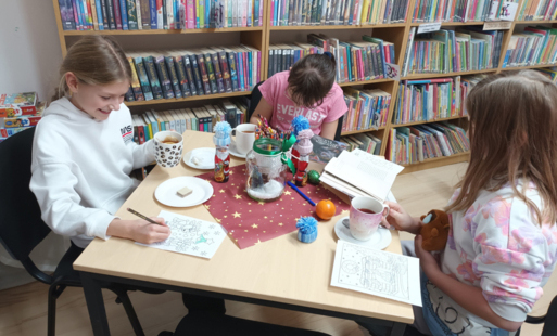dzieci siedzą przy stole w bibliotece i robią rękodzieło tj malują