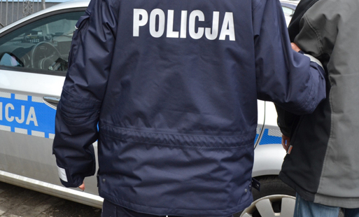 zatrzymany stoi obok radiowozu, trzymany przez policjanta, obaj stoją tyłem