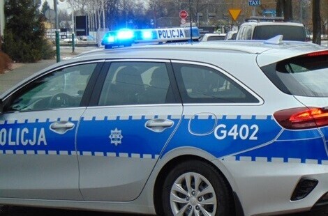 radiowóz z odpalonymi światłami na tle ulicy