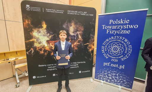 Szymon Gałuszka pozuje z duplomem na tle baneru