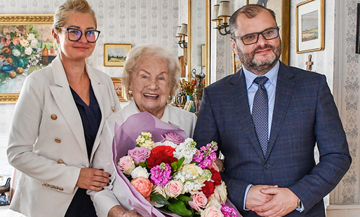 pani Leokadia Wójcik stoi w środku w swoim salonie, trzyma bukiet kwiatów, po jej lewej stronie, a prawej stronie widza stoi burmistrz gminy Kęty, po prawej stronie p. Jachimczak-Zinkowska, zastępca kierownika Usc