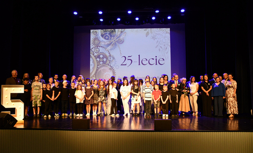 dzieci, absolwenci stoją na scenie Domu Kultury na tle napisu 25 lat 