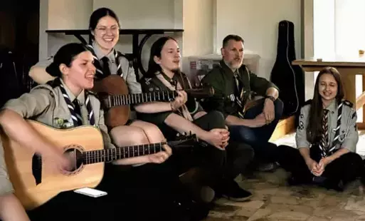Pięcioro dorosłych harcerzy podczas wspólnego śpiewania, dwie z harcerek grają na gitarze