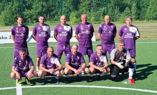 na tle lasku i stadionu pozują zawodnicy Hejnału Kęty Oldboys, ubrani w swoje charakterystyczne fioletowe stroje