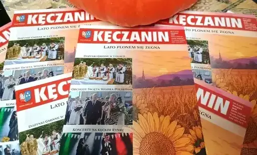 Kilka gazet "Kęczanin" rozsypanych na stole, powyżej dynia